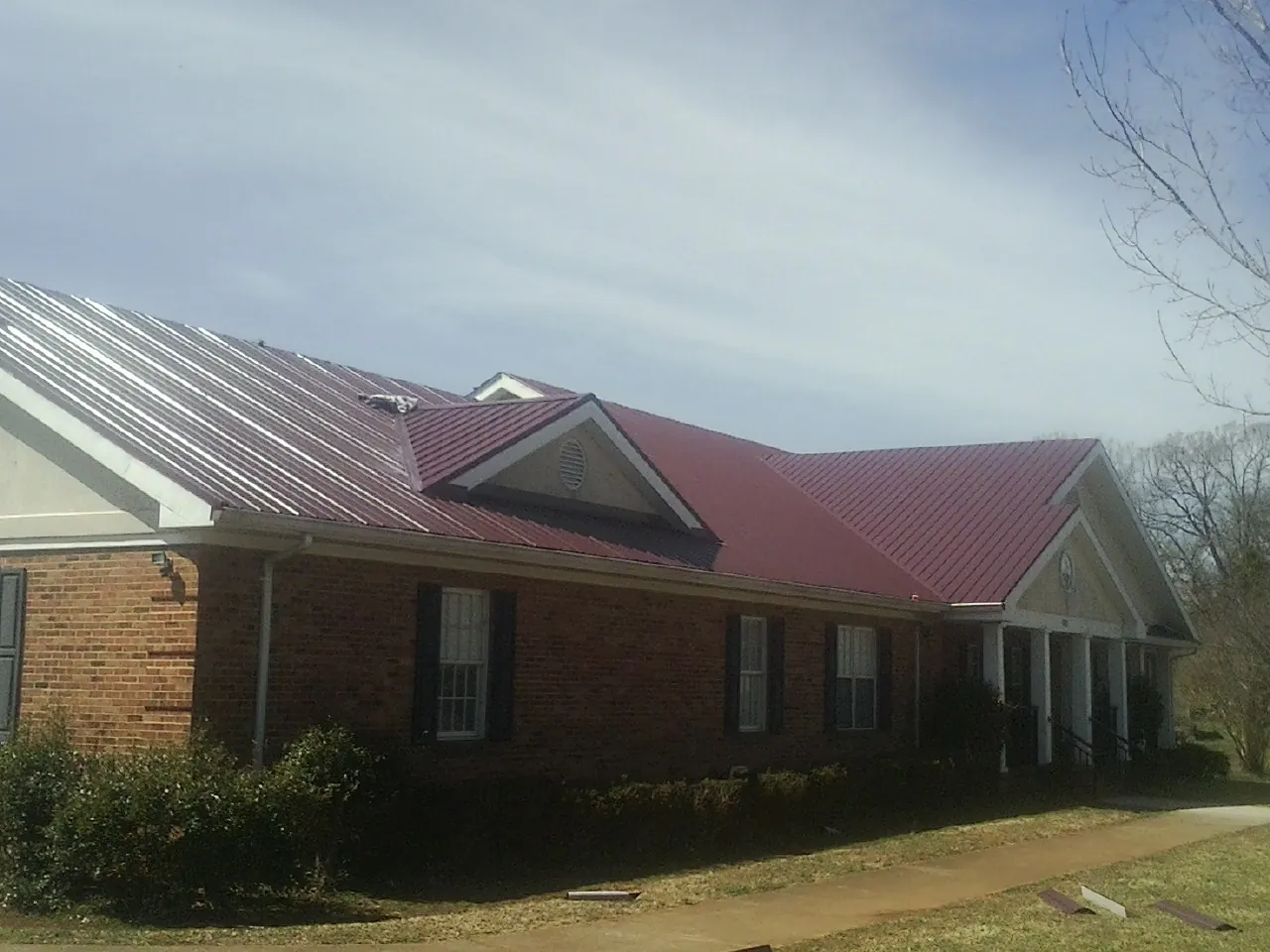 Red metal roof with gabled entries on a long brick building, from a Hail Damage Roof Repair job in Napa